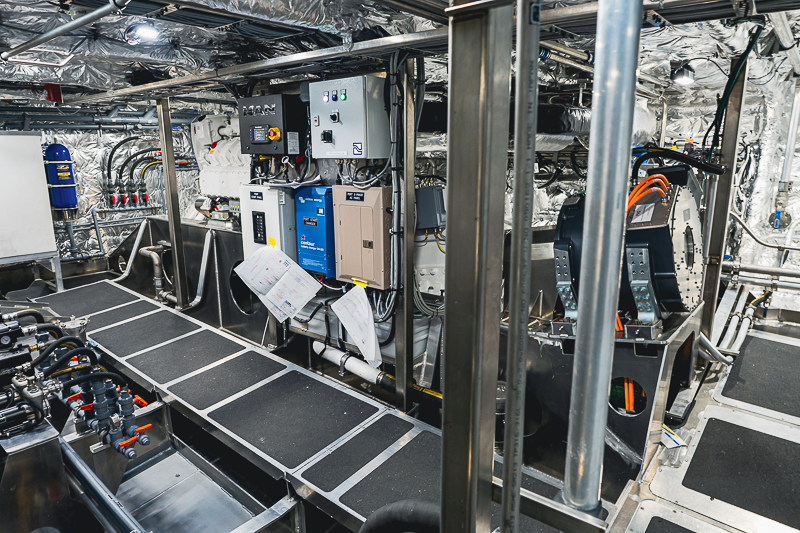 HBC_El Escudo_Marketing_Onboard_Web-1 Industrial engine room with control panels, cables, and metal walkways; foil-insulated walls and assorted machinery nearby.