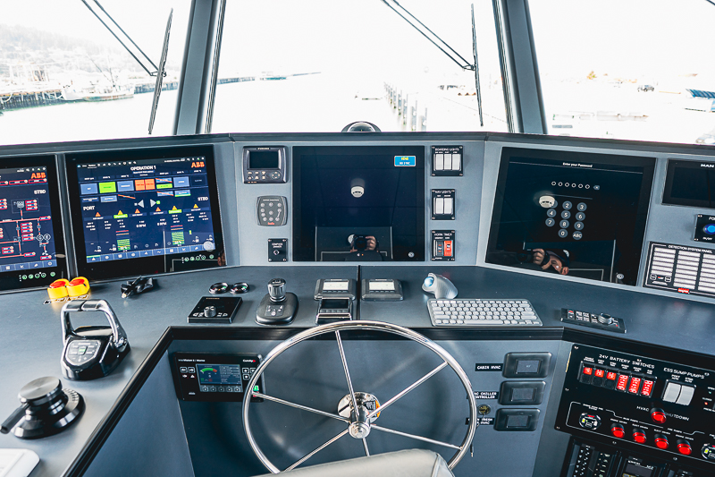 HBC_El Escudo_Marketing_Onboard_Web-18 Bridge of a modern vessel with a stainless steering wheel and multiple navigation screens at the helm station