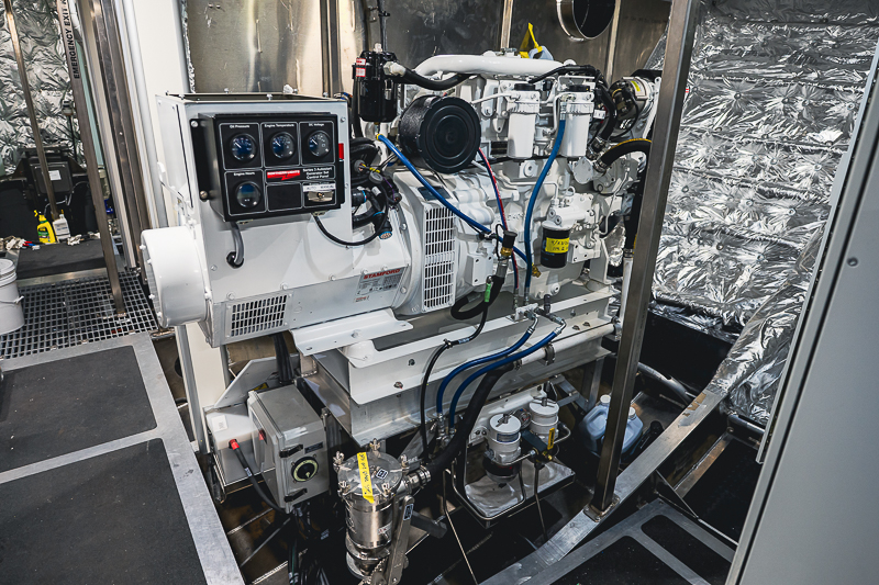 HBC_El Escudo_Marketing_Onboard_Web-19 Industrial diesel engine in a metal enclosure with a control panel, gauges, and blue hoses.