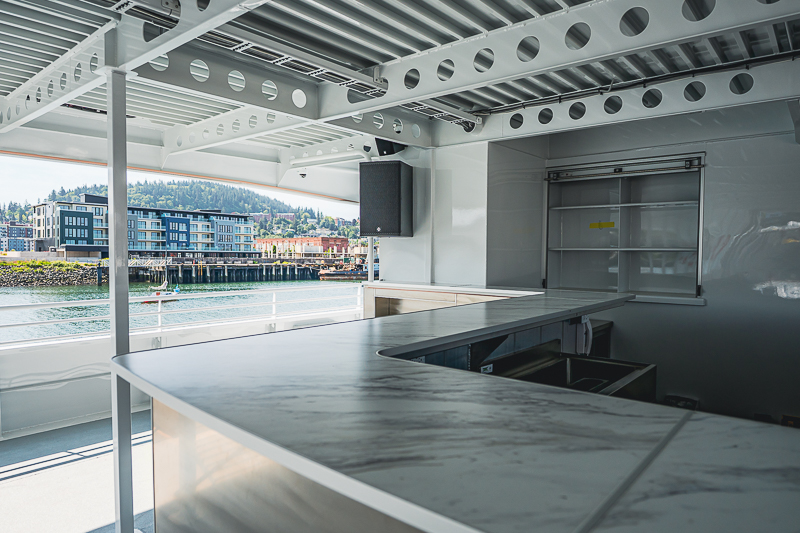 HBC_El Escudo_Marketing_Onboard_Web-3 Open-air ship bar with a marble counter and exposed steel framework, overlooking the harbor.