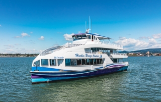 Large white and blue cruise boat named Harbor Breeze Cruises on calm harbor water with a distant shoreline.