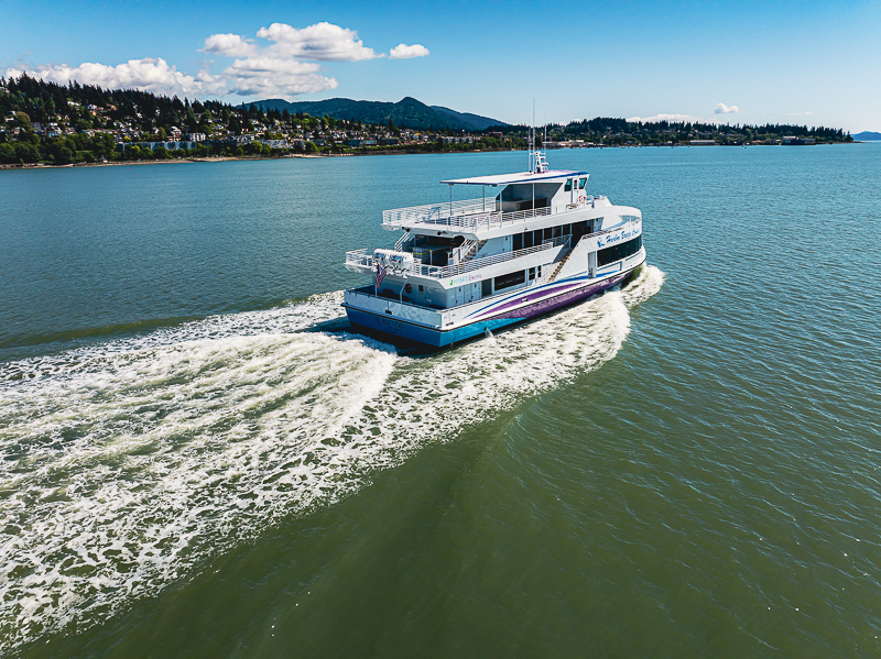 default White multi-deck passenger ferry cruising on blue water near a coastal town.