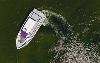 Aerial view of a white speedboat with a purple canopy cruising in green water, leaving a wake behind it.