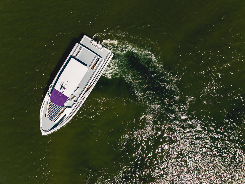 Aerial view of a white speedboat with a purple canopy cruising in green water, leaving a wake behind it.