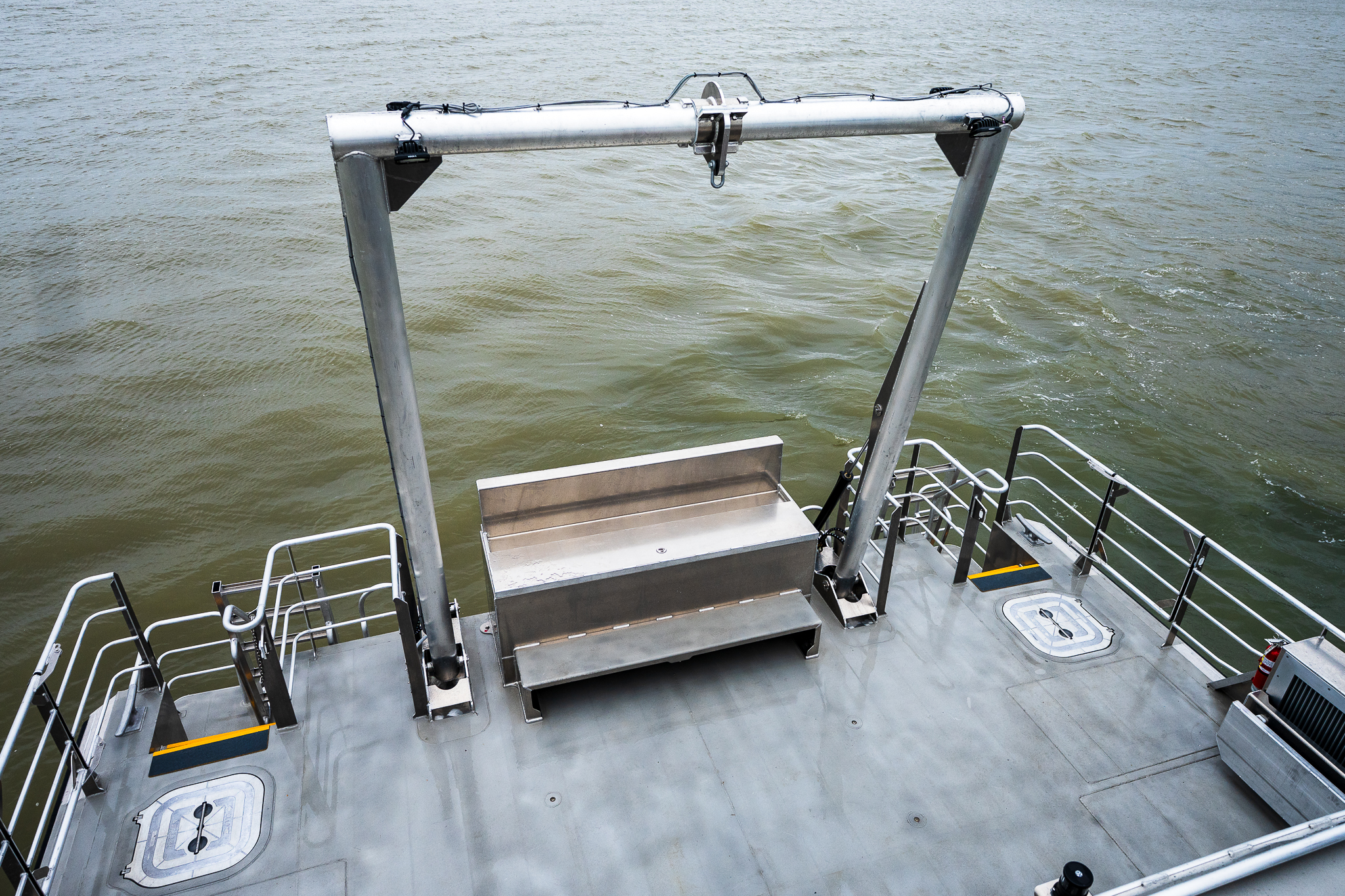 Metal loading platform and davit frame on a boat deck with choppy water in the background.