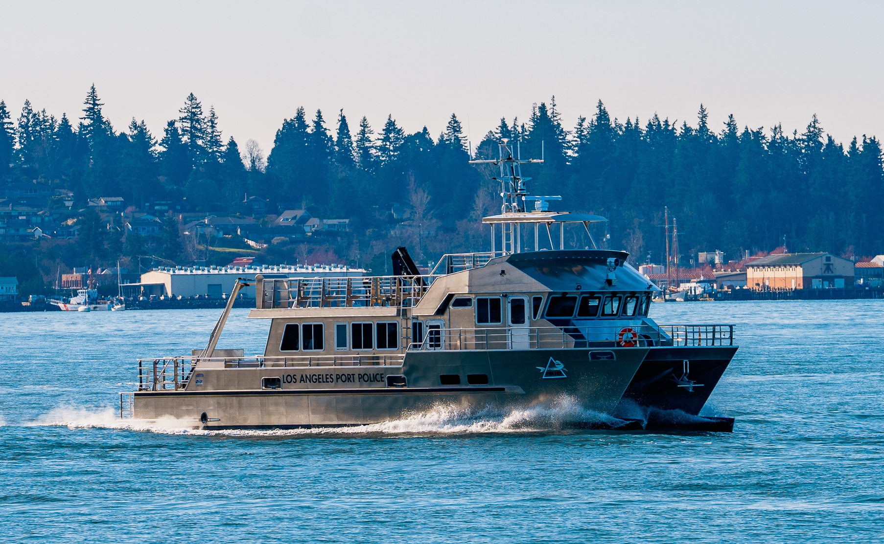 Los Angeles Port Police boat cruising through blue harbor with a tree-lined shoreline in the background.