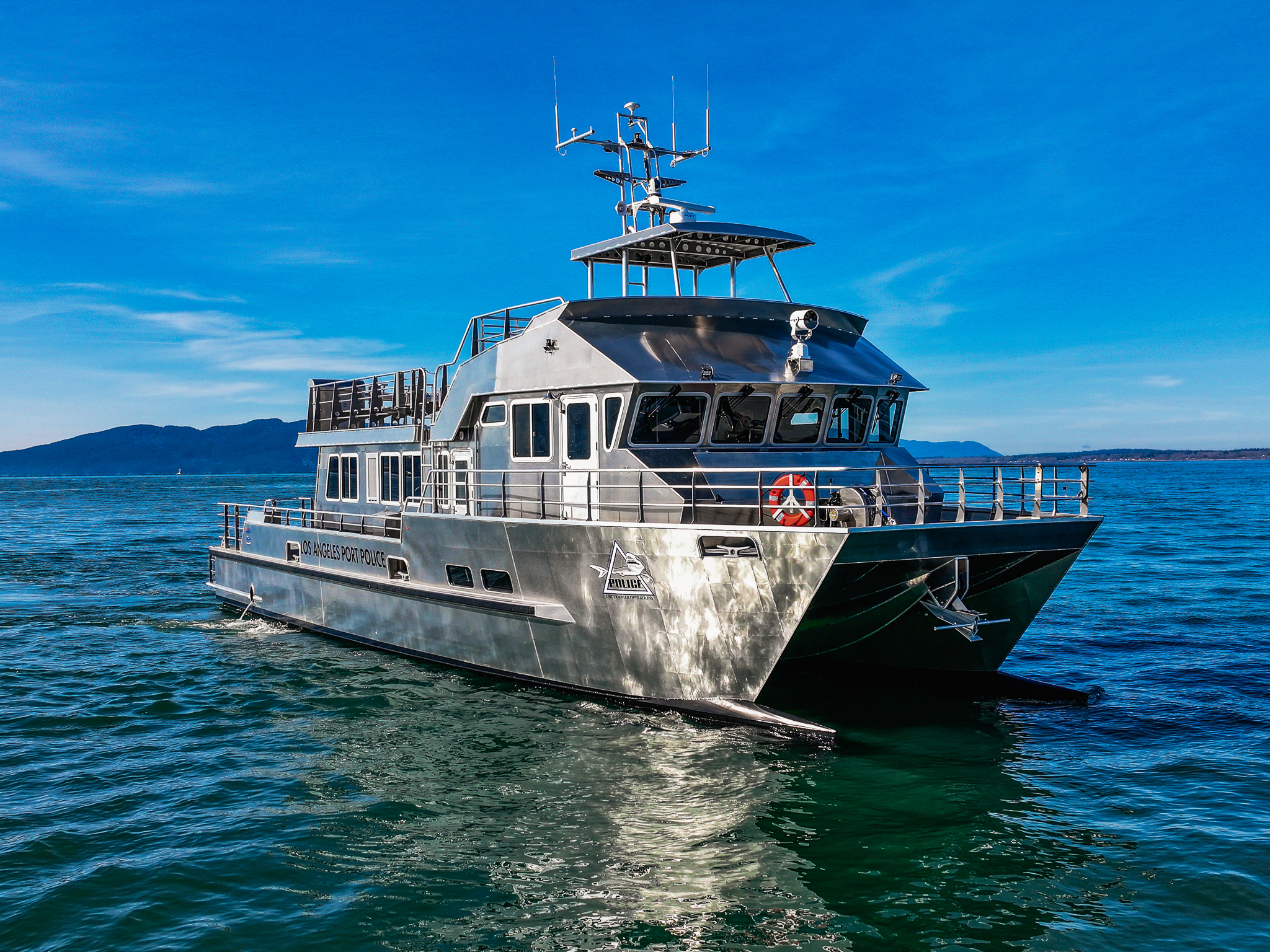 Metal police boat docked on calm blue water with clear sky and distant hills on the horizon.