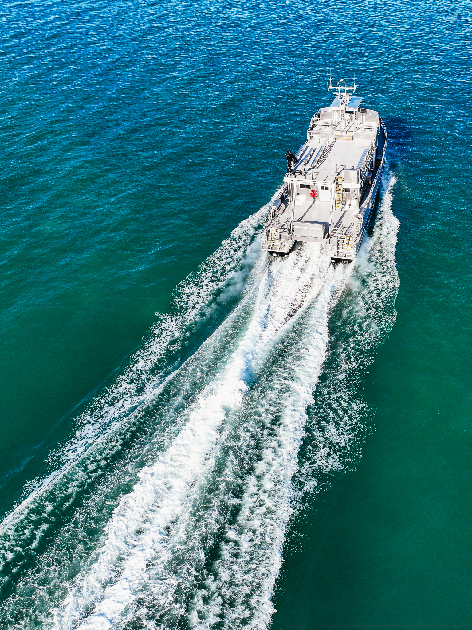 Aerial view of a gray motorboat cruising through turquoise water, leaving a foamy white wake behind it.