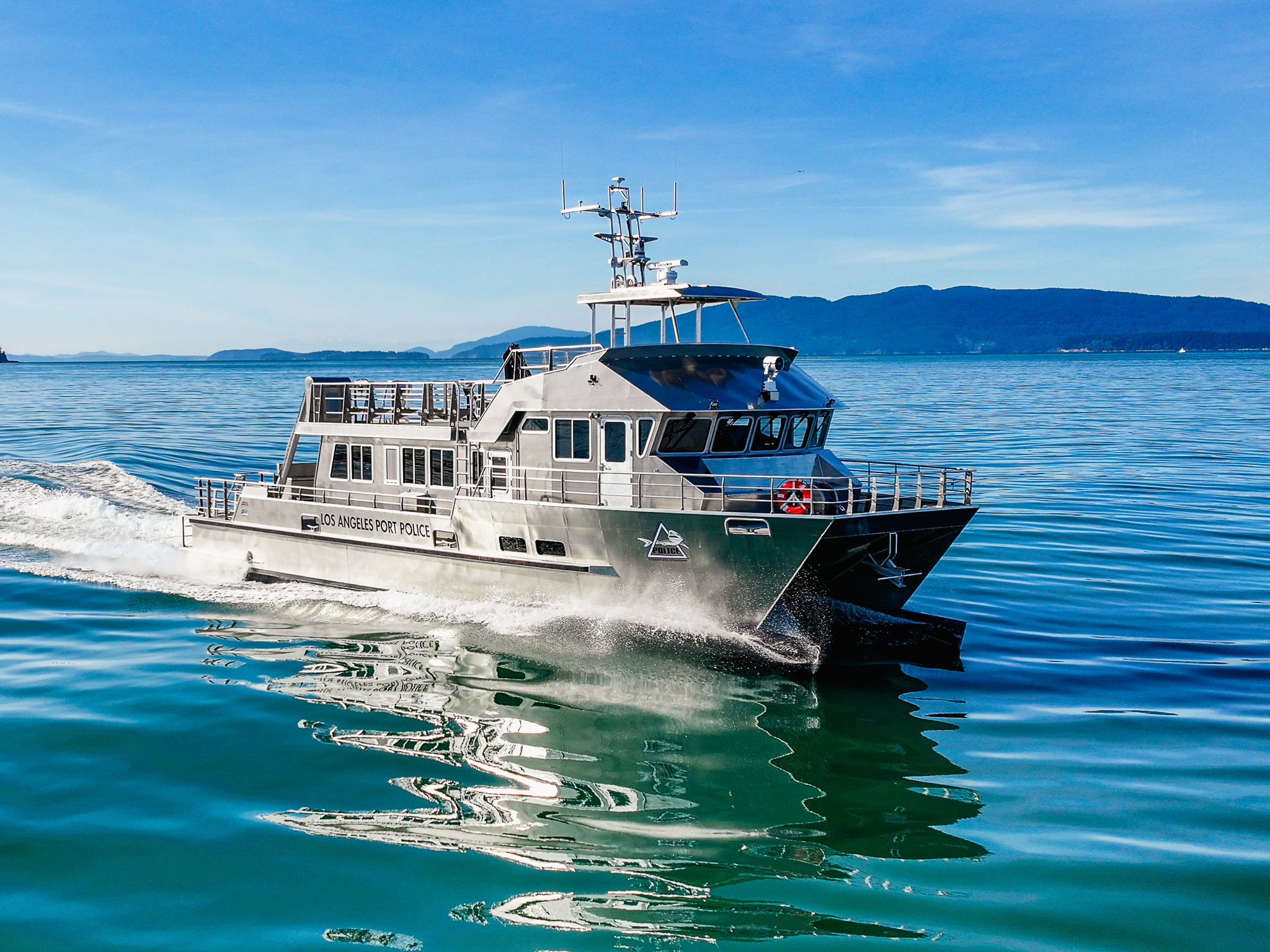 Los Angeles Port Police boat sailing on calm blue water with mountains in the distance under a clear sky.