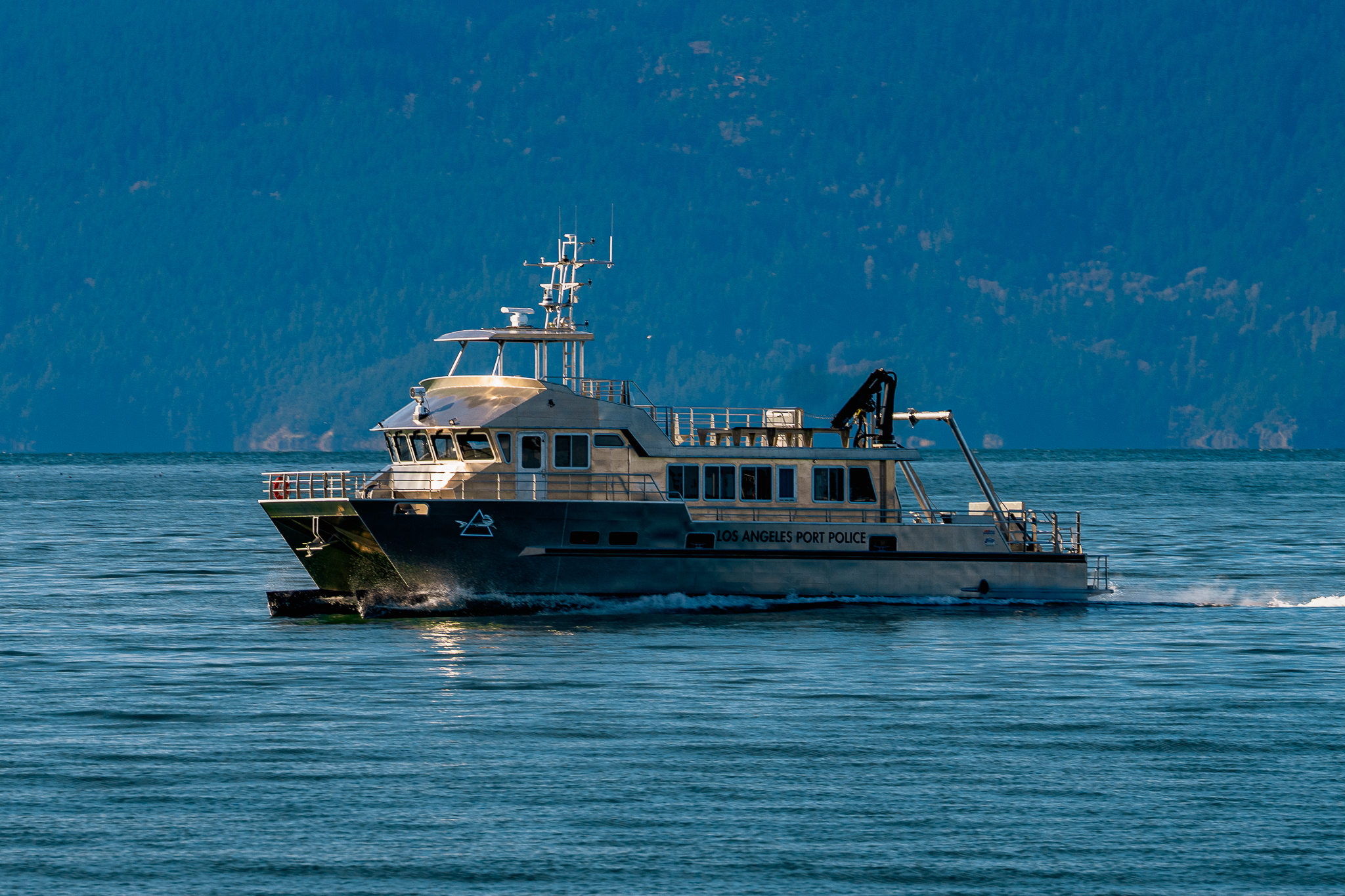 Los Angeles Port Police patrol boat on calm blue water with forested mountains in the background.